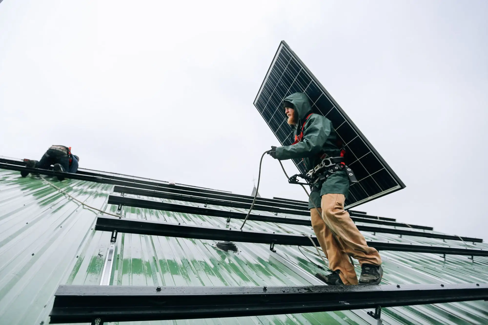 Installer carrying a solar panel across a metal roof