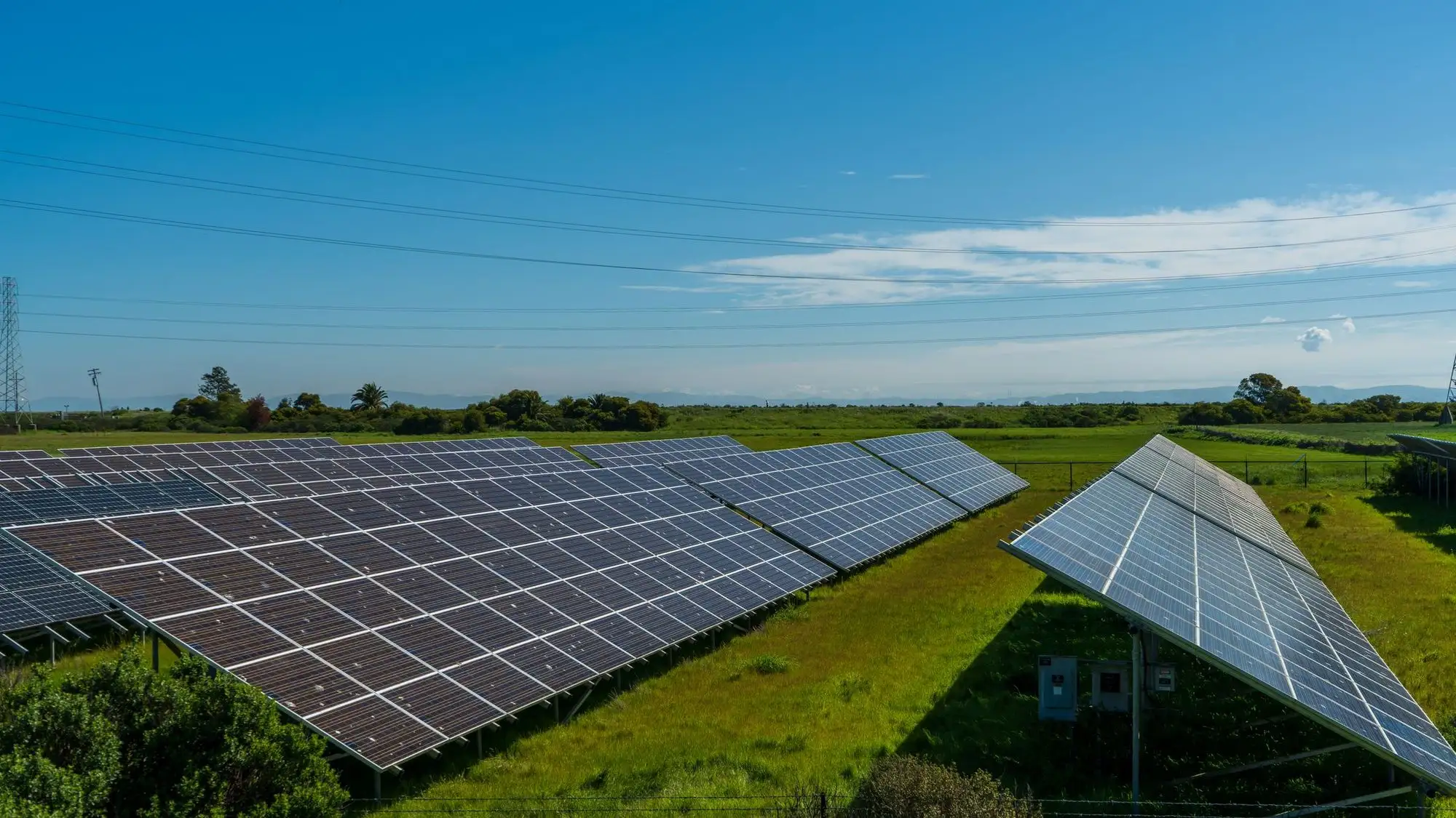 Ground-mounted solar arrays on green farmland under a clear sky